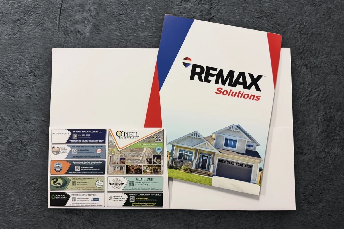 Custom RE/MAX Solutions presentation folder, open to show local vendor ads printed on the pocket